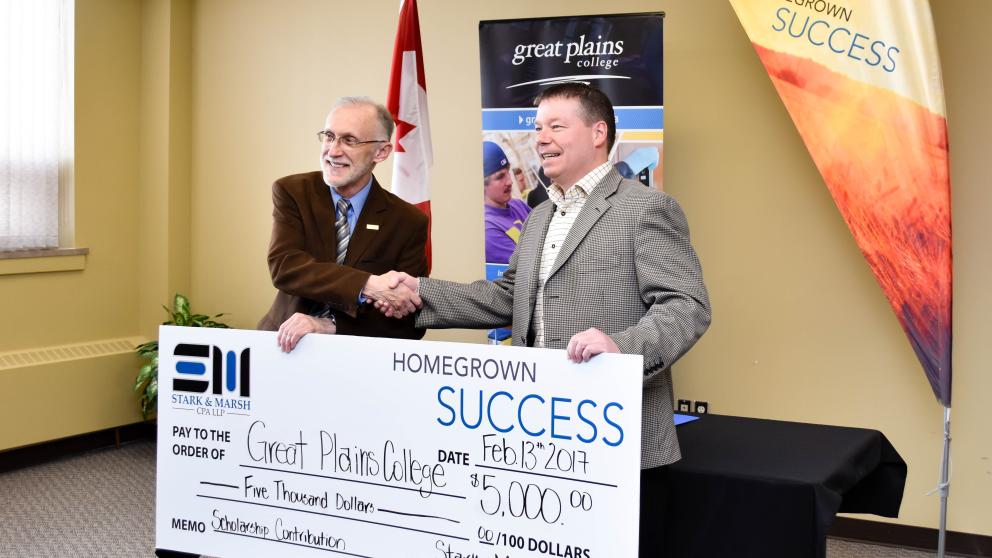 two men shaking hands with a very large cheque