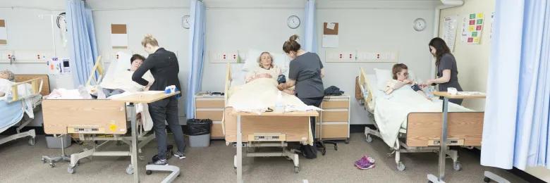 Nursing lab set up with three beds and students completing a lab