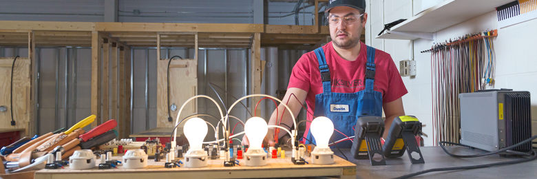 An electrician student in the electric shop, standing at his work bench with an electrical board